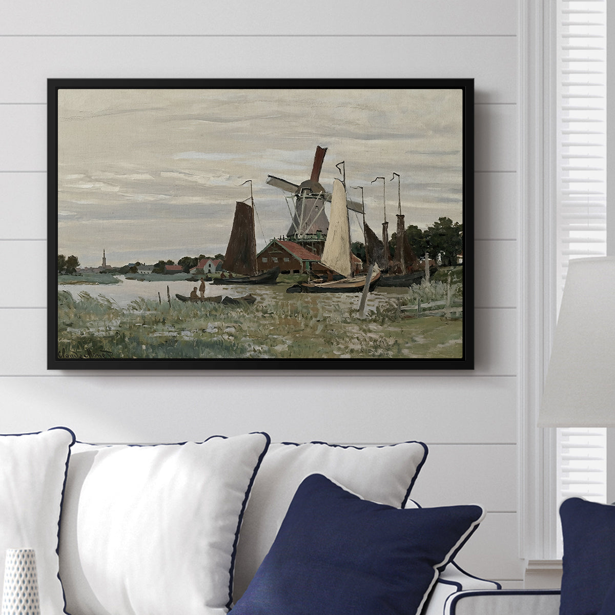 Windmill at Zaandam, 1871 by Claude Monet displayed above a sofa in a living room in a black floater frame, featuring an impressionist depiction of windmill near riverbank.