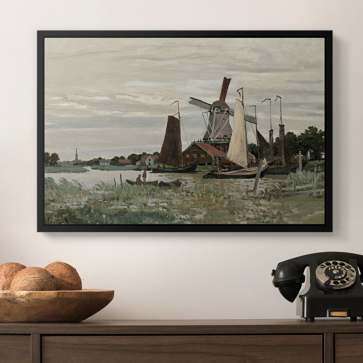 Windmill at Zaandam, 1871 by Claude Monet in a black floater framed canvas displayed above a console table in a hallway, featuring a countryside structure standing against open sky.