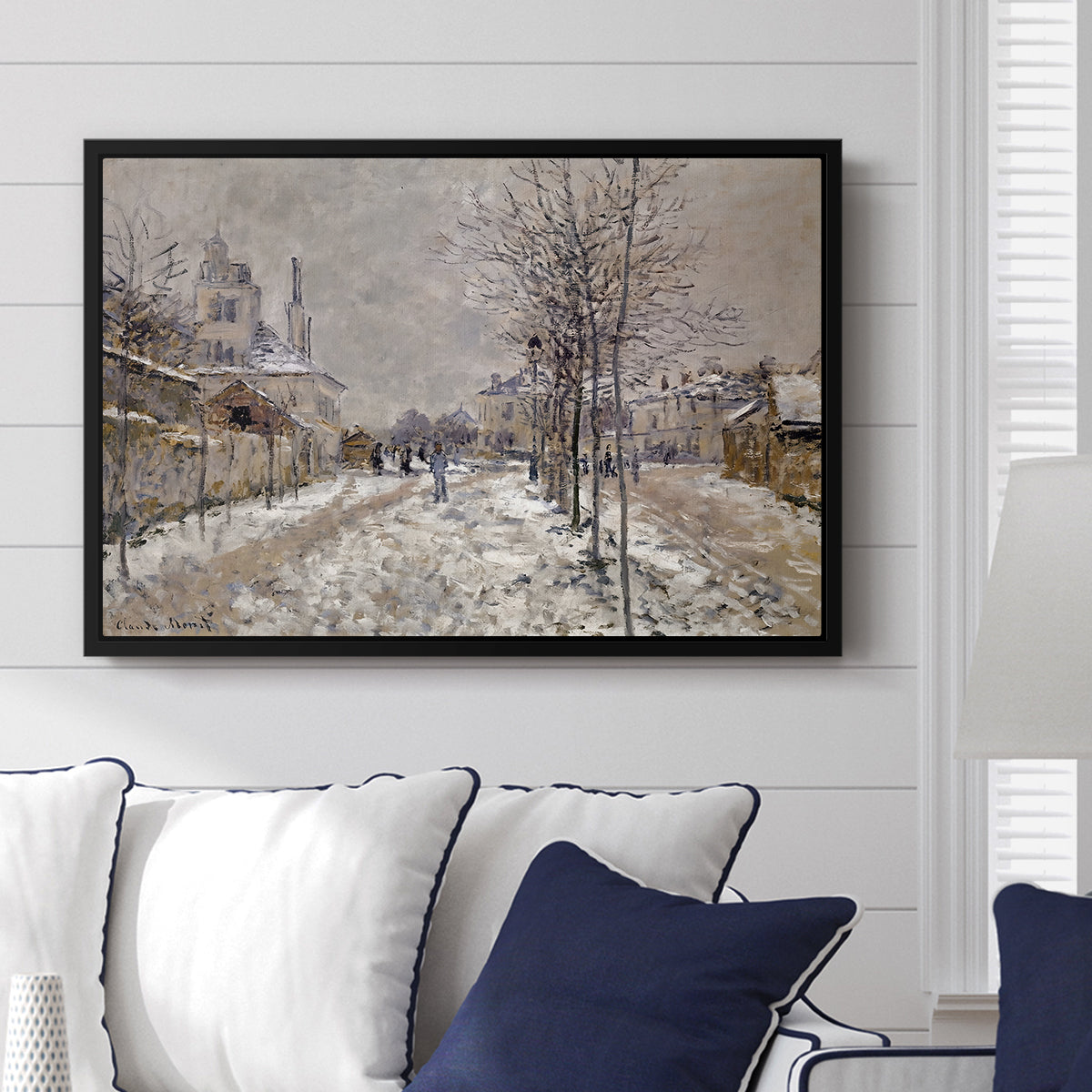 The Boulevard de Pontoise at Argenteuil, Snow Effect, 1875 by Claude Monet displayed above a sofa in a living room in a black floater frame, featuring an impressionist winter scene with road and bare trees.