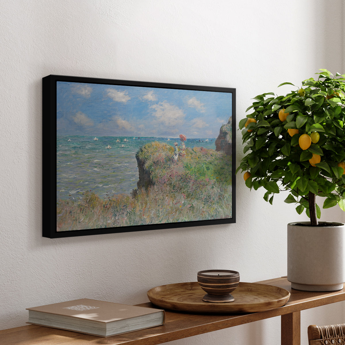 The Cliff Walk at Pourville, 1882 by Claude Monet, presented in a black floater framed canvas featuring figures walking along coastal cliff path overlooking ocean and sky, displayed above a hallway console table.