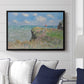 The Cliff Walk at Pourville, 1882 by Claude Monet displayed above a sofa in a living room in a black floater frame, featuring an impressionist seaside landscape with people strolling above water.