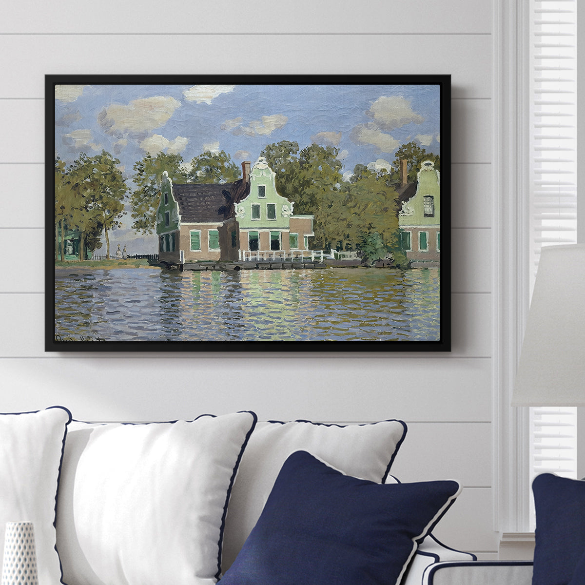 Houses on the Zaan River at Zaandam, 1871 by Claude Monet displayed above a sofa in a living room in a black floater frame, featuring an impressionist riverside village with colorful buildings.