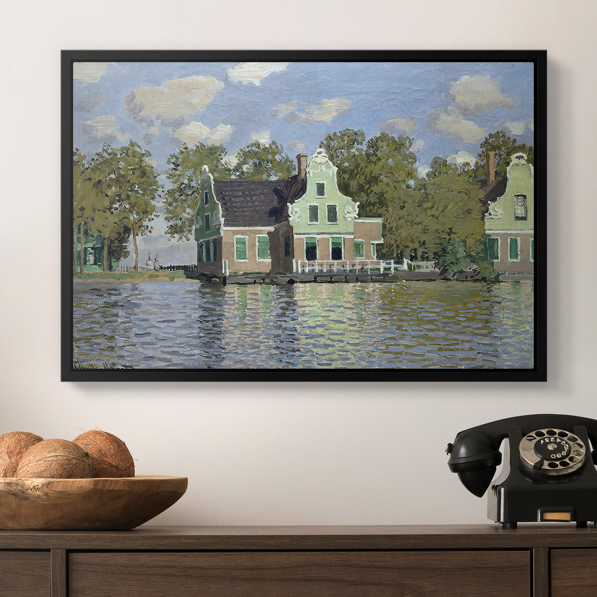 Houses on the Zaan River at Zaandam, 1871 by Claude Monet in a black floater framed canvas displayed above a console table in a hallway, featuring a waterfront architecture with still reflections.