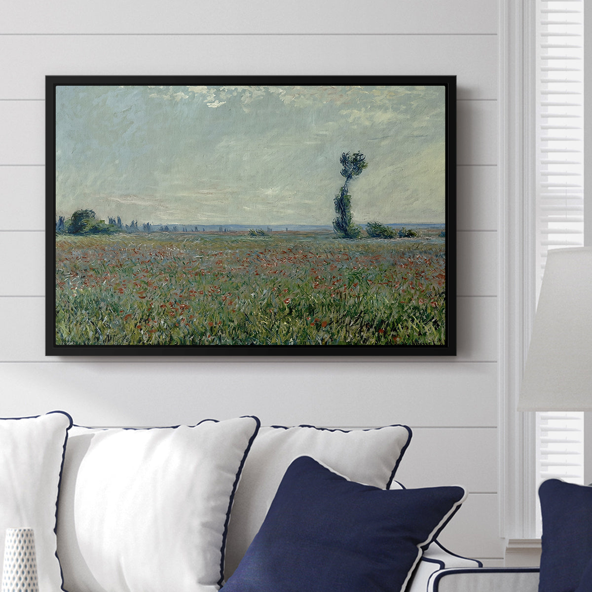 Poppy Field, 1881 by Claude Monet displayed above a sofa in a living room in a black floater frame, featuring an impressionist landscape filled with blooming flowers and greenery.