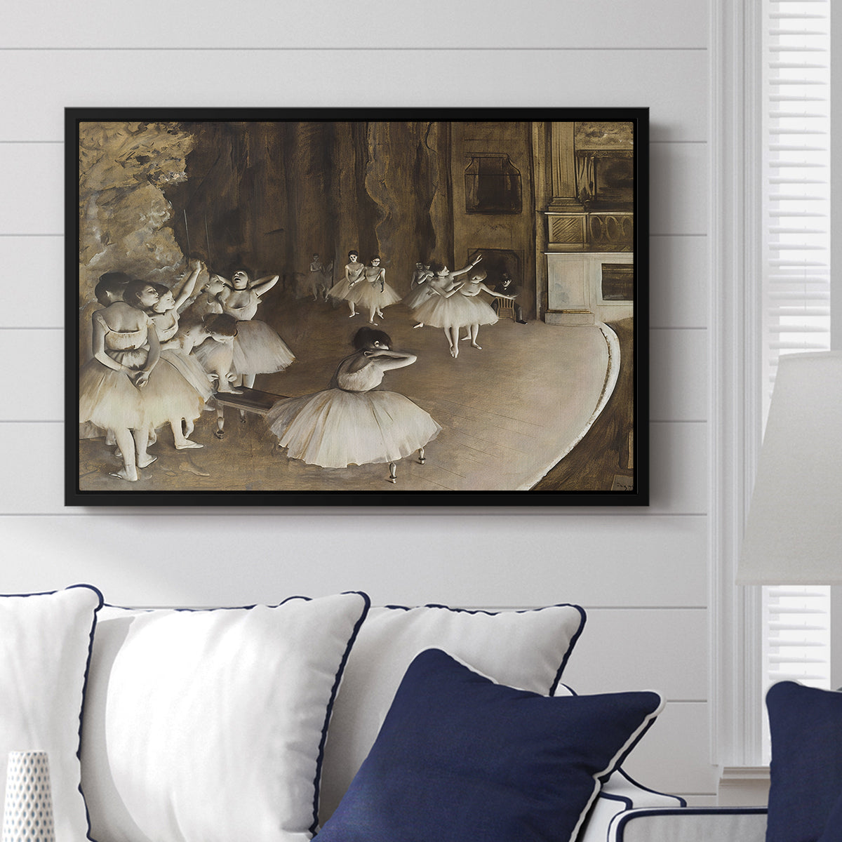 The Rehearsal of the Ballet Onstage, 1874 by Edgar Degas displayed above a sofa in a living room in a black floater frame, featuring a stage rehearsal scene with dancers preparing performance.