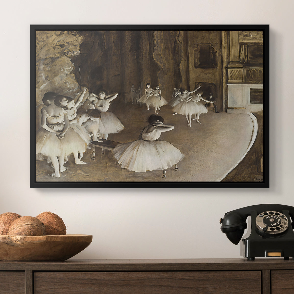 The Rehearsal of the Ballet Onstage, 1874 by Edgar Degas in a black floater framed canvas displayed above a console table in a hallway, featuring dancers arranged on stage with visible set and depth.