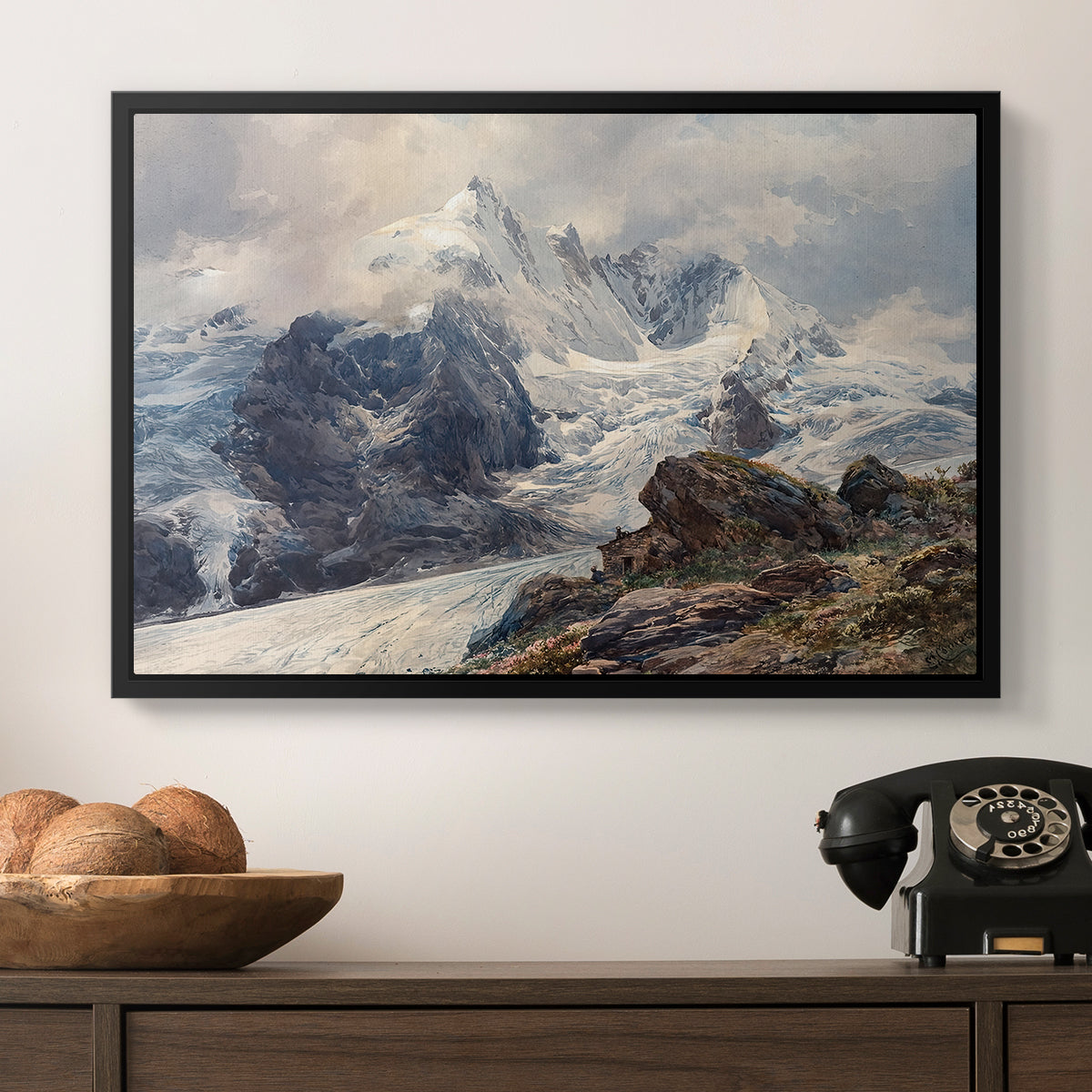 The Grossglockner, 1880 by Edward Theodore Compton in a black floater framed canvas displayed above a console table in a hallway, featuring an alpine peak dominating surrounding terrain.