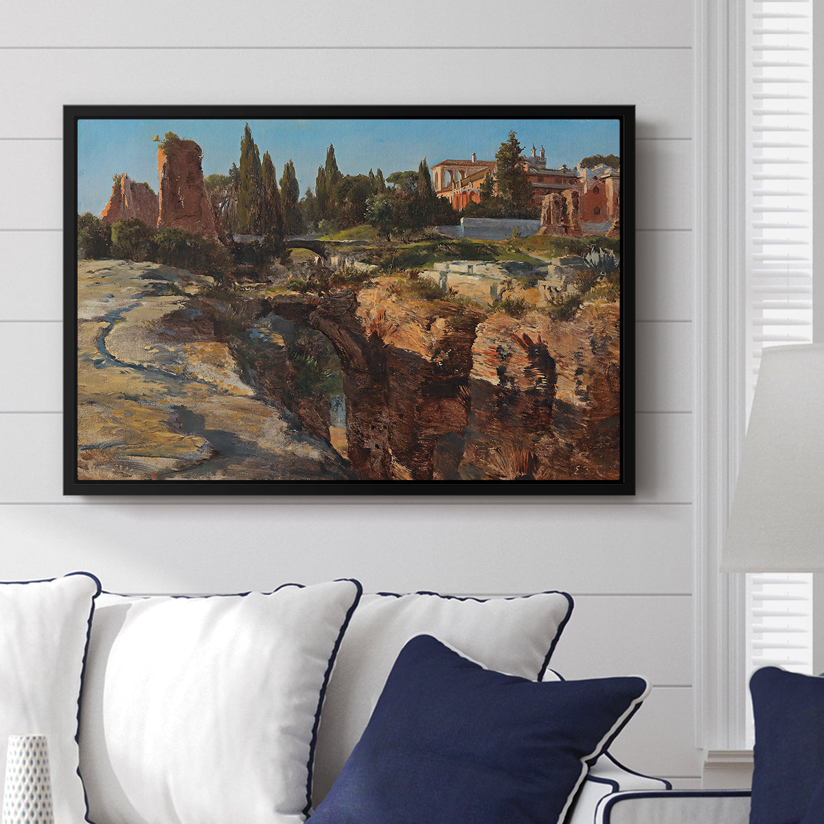 Palatine in Rome, c. 1921 by Edward Theodore Compton displayed above a sofa in a living room in a black floater frame, featuring an architectural scene of ancient structures in sunlit environment.