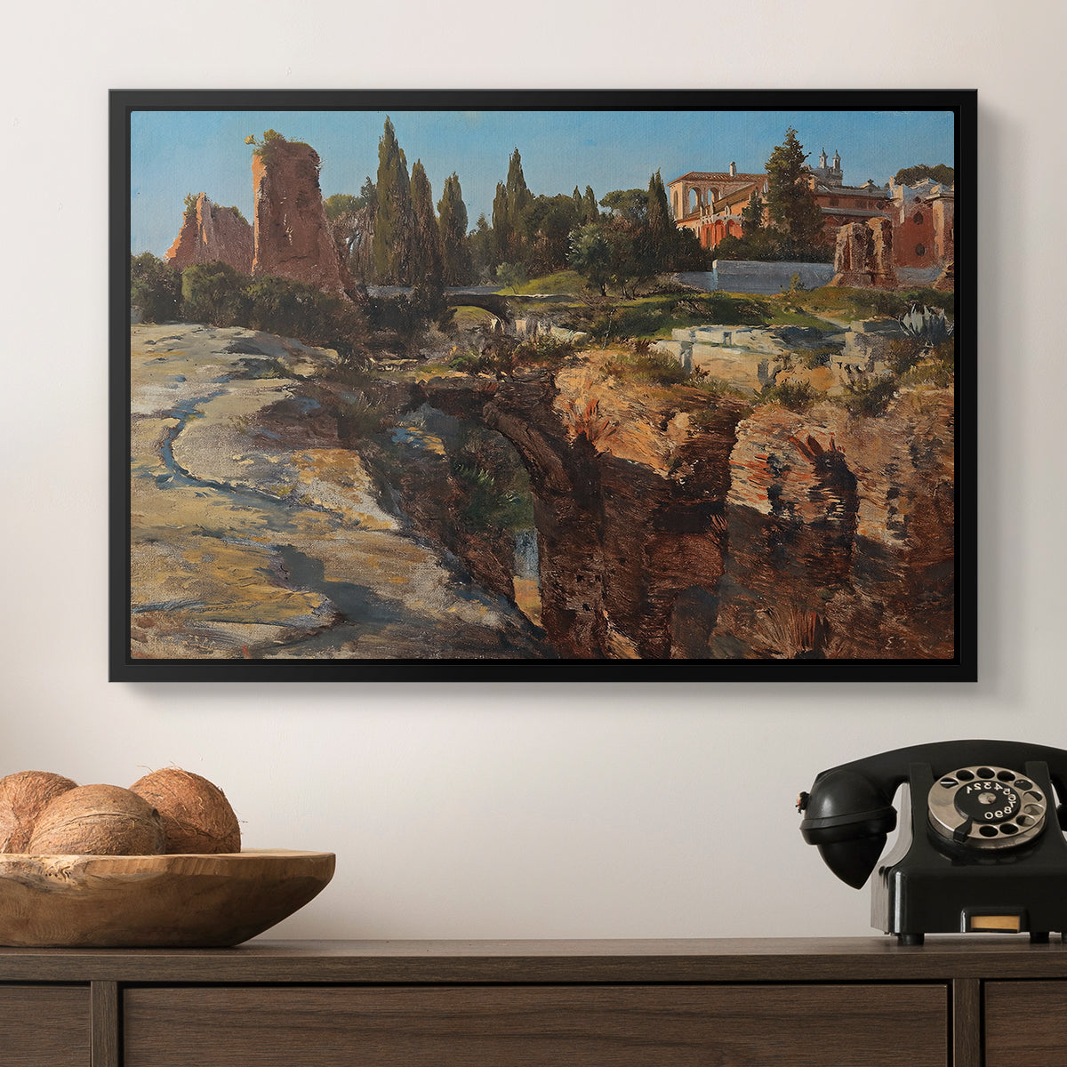Palatine in Rome, c. 1921 by Edward Theodore Compton in a black floater framed canvas displayed above a console table in a hallway, featuring a detailed depiction of historic Roman architecture.