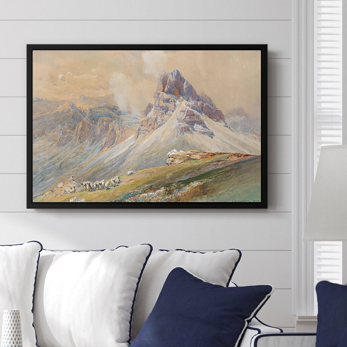 From the Dolomites, 1904 by Edward Theodore Compton displayed above a sofa in a living room in a black floater frame, featuring an alpine scene with jagged rock formations and distant mountains.
