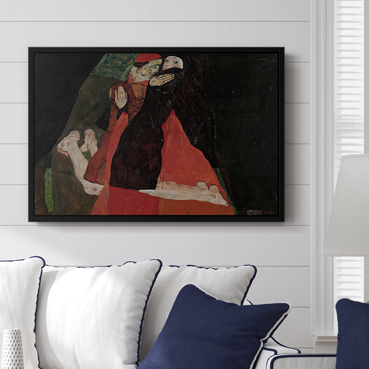 Cardinal and Nun (Caress), 1912 by Egon Schiele displayed above a sofa in a living room in a black floater frame, featuring a cardinal and nun depicted in close emotional interaction.
