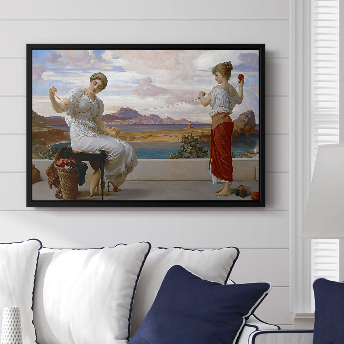 Winding the Skein, c. 1878 by Frederic Leighton displayed above a sofa in a living room in a black floater frame, featuring two women engaged in textile work with draped garments.