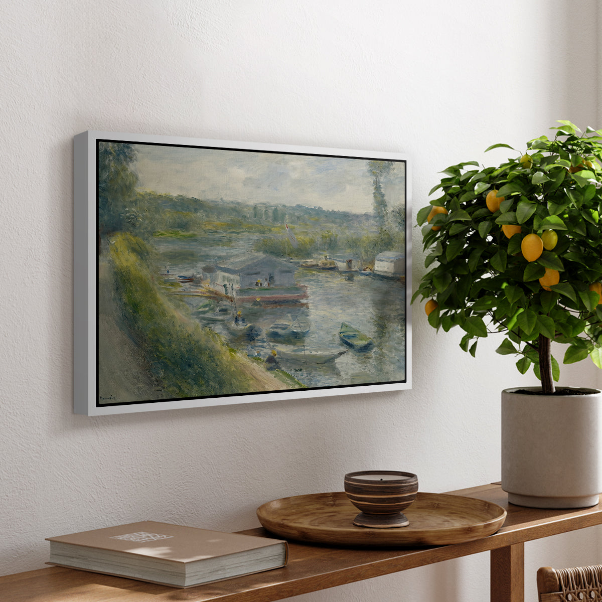 Wash-House Boat at Bas-Meudon, c. 1874 by Pierre-Auguste Renoir, presented in a white floater framed canvas featuring a floating wash-house boat along a riverbank with figures working nearby, displayed above a hallway console table.