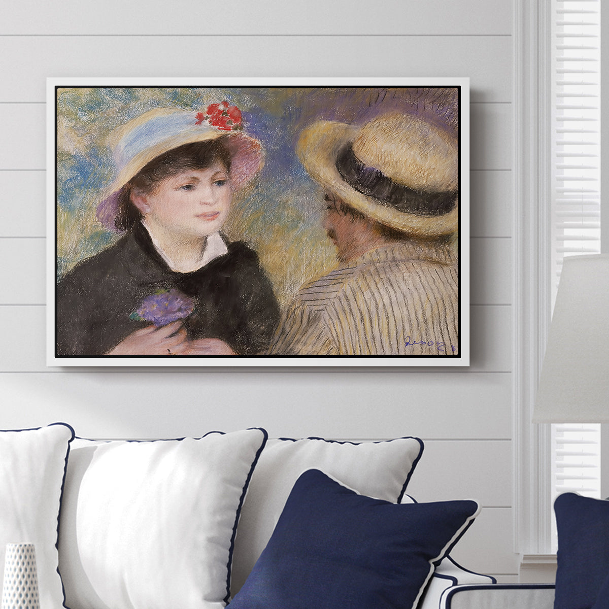 Boating Couple (Aline Charigot and Renoir), c. 1881 by Pierre-Auguste Renoir displayed above a sofa in a living room in a white floater frame, featuring an intimate portrait of man and woman sitting side by side in outdoor setting.