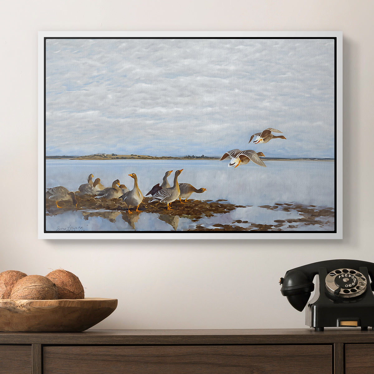 Greylag Geese (Grågäss), 1922 by Bruno Liljefors in a white floater framed canvas displayed above a console table in a hallway, featuring a flock of geese positioned along marshy terrain.
