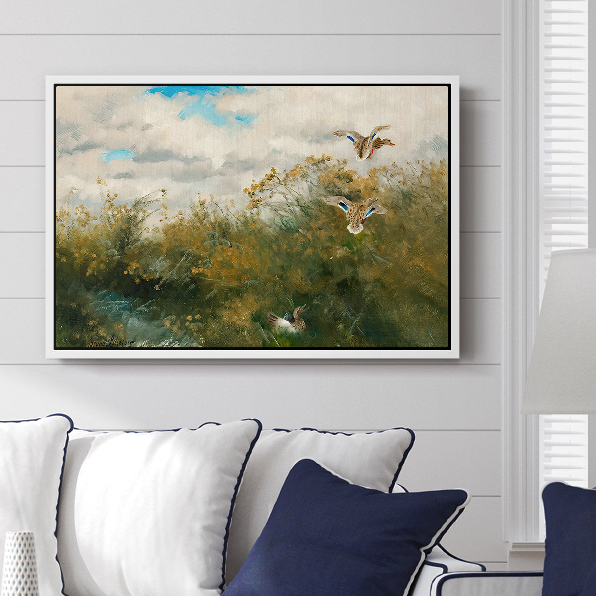 Wild Ducks (Grasänder), 1890 by Bruno Liljefors displayed above a sofa in a living room in a white floater frame, featuring a wildlife scene of ducks walking through tall grass beside water.