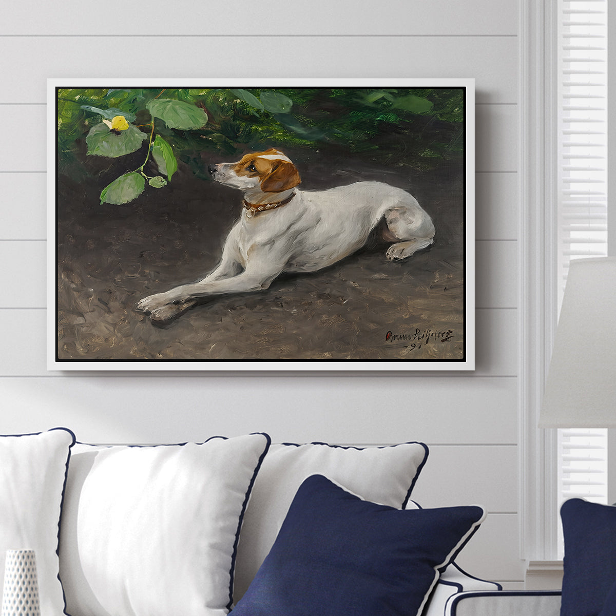 Portrait of a Dog, 1891 by Bruno Liljefors displayed above a sofa in a living room in a white floater frame, featuring a realistic portrait of a resting dog with attentive expression.