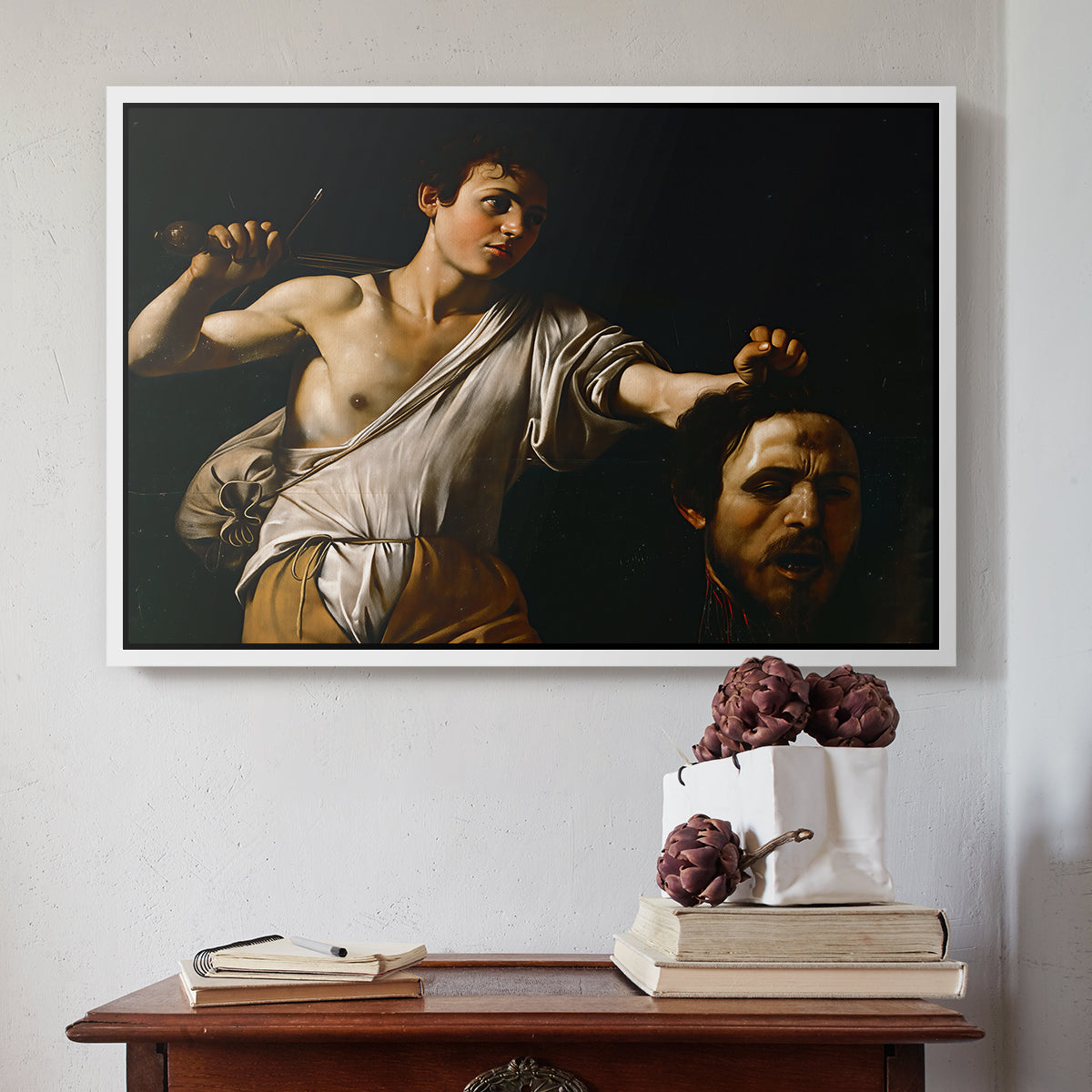 White floater framed canvas featuring David with the Head of Goliath (Vienna Version), c. 1607 by Caravaggio above an entryway table in a minimalist foyer.
