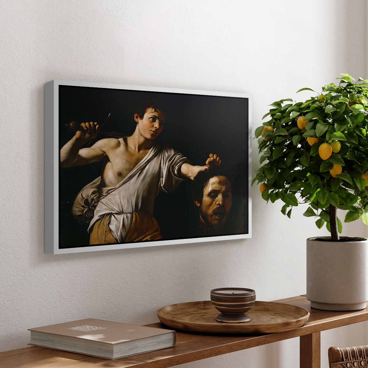 David with the Head of Goliath (Vienna Version), c. 1607 by Caravaggio, presented in a white floater framed canvas featuring a young David holding the severed head of Goliath against a dark background, displayed above a hallway console table.