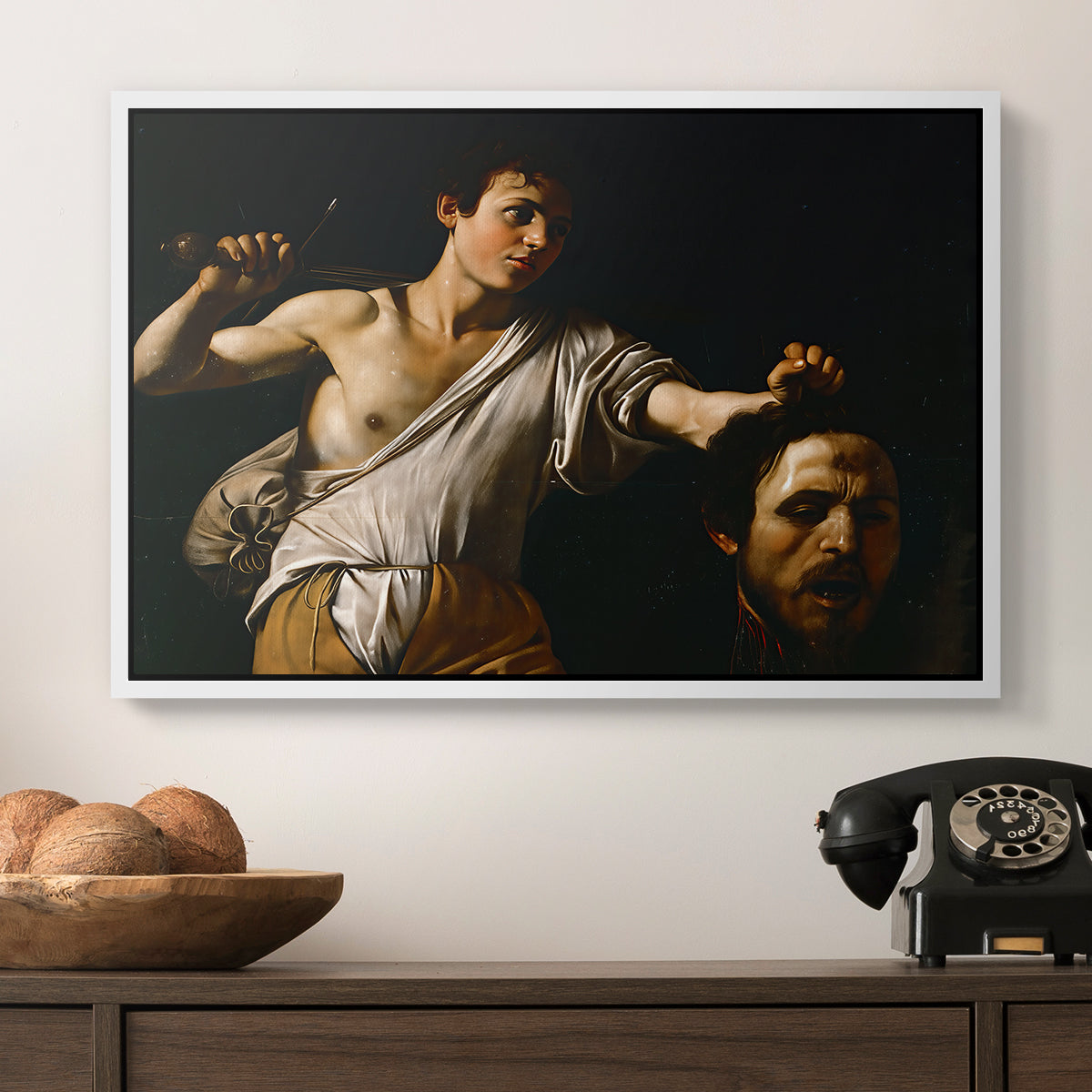 David with the Head of Goliath (Vienna Version), c. 1607 by Caravaggio in a white floater framed canvas displayed above a console table in a hallway, featuring an intense religious scene with figure emerging from darkness holding trophy.