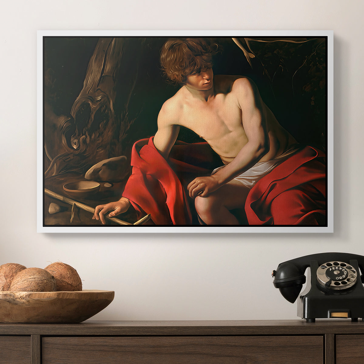 Saint John the Baptist in the Wilderness, c. 1603-1604 by Caravaggio in a white floater framed canvas displayed above a console table in a hallway, featuring a contemplative religious figure in rustic wilderness environment.