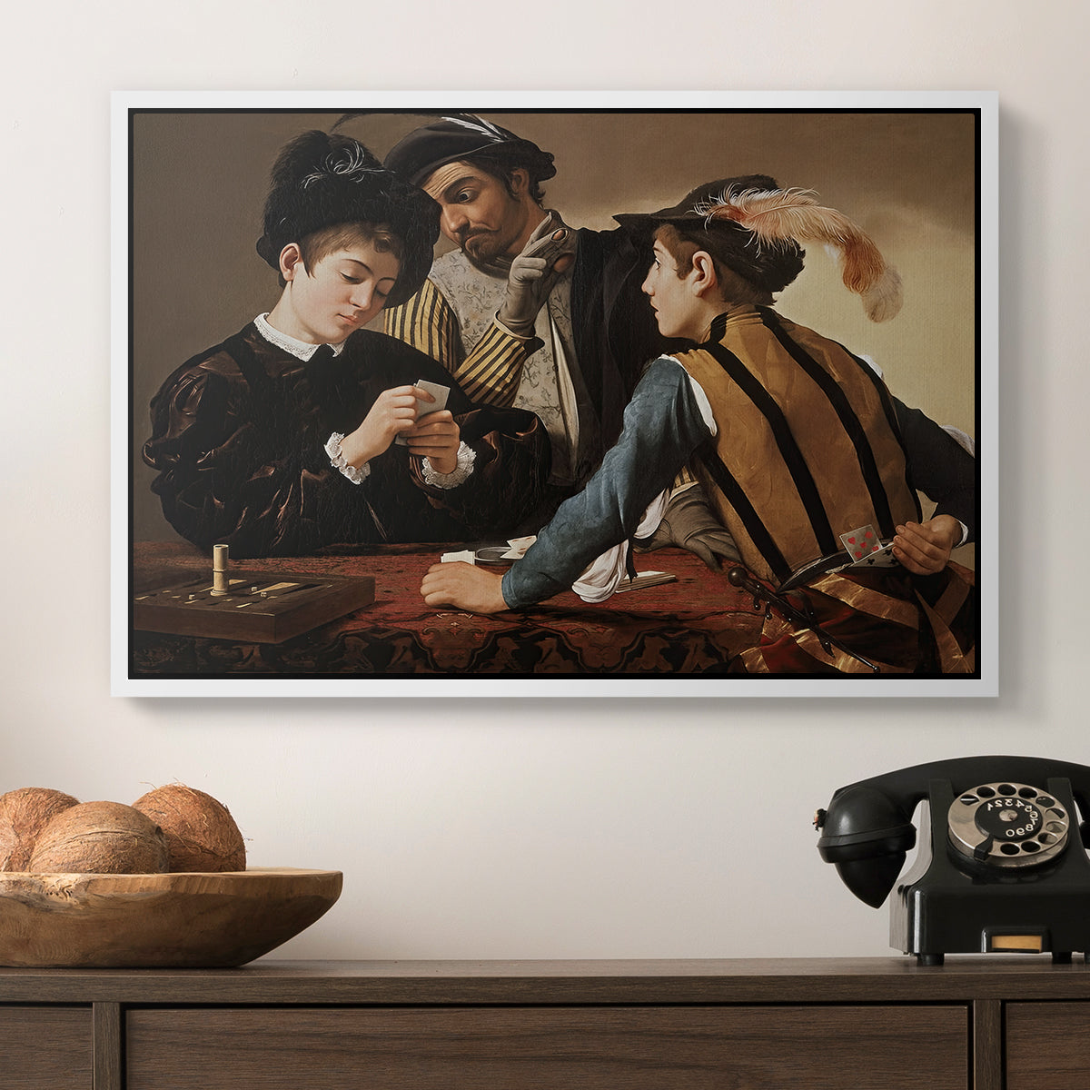 The Cardsharps, c. 1594 by Caravaggio in a white floater framed canvas displayed above a console table in a hallway, featuring a dramatic interior scene of gambling and trickery among figures.