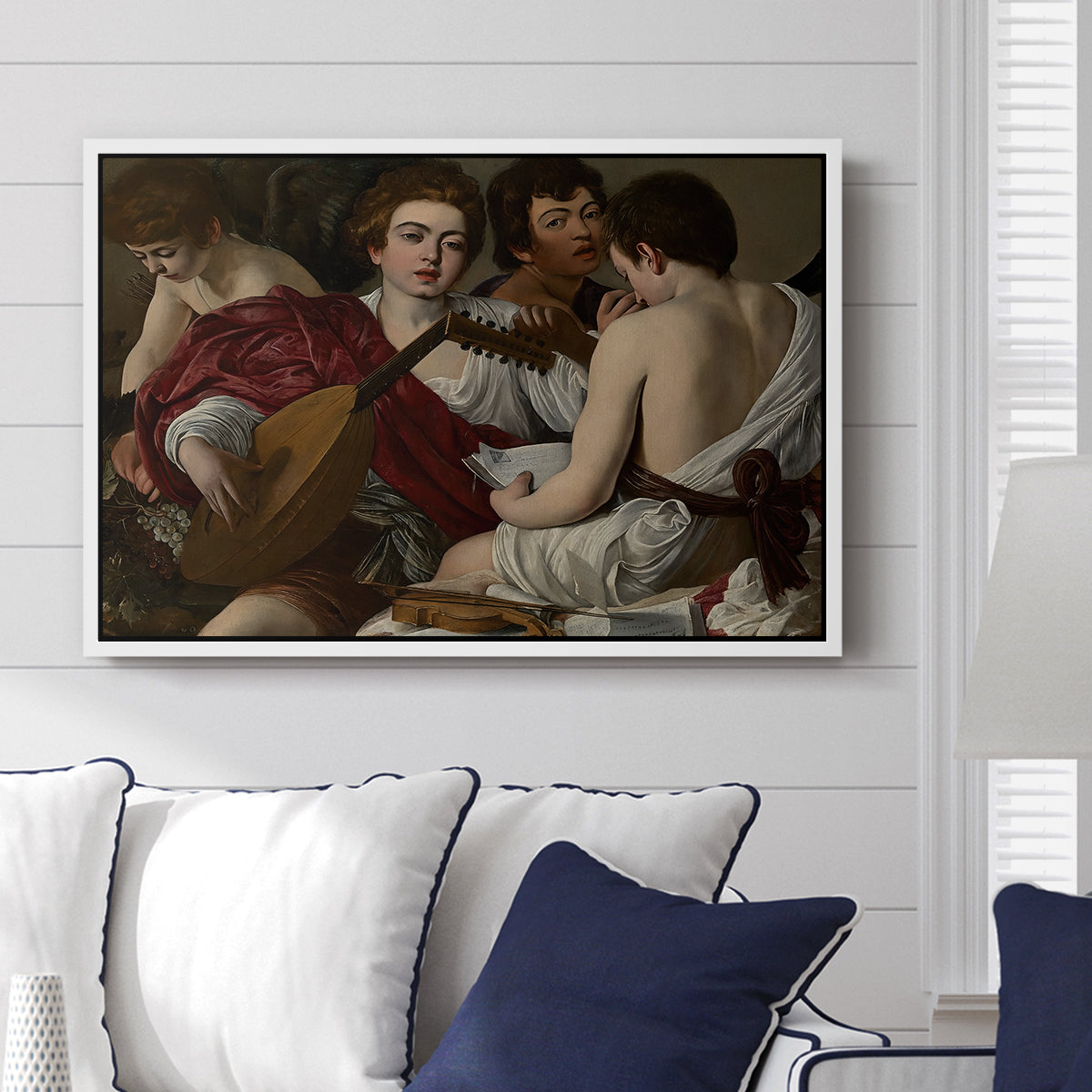 The Musicians, c. 1595 by Caravaggio displayed above a sofa in a living room in a white floater frame, featuring an ensemble of musicians holding lute and singing in close arrangement.