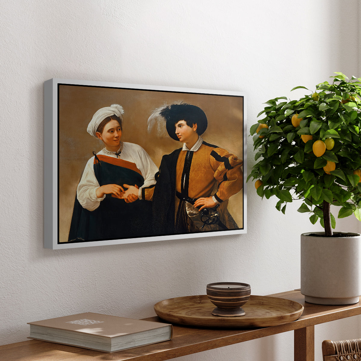 The Fortune Teller (Capitoline Version), c. 1599 by Caravaggio, presented in a white floater framed canvas featuring a woman reading man's palm while discreetly removing his ring, displayed above a hallway console table.