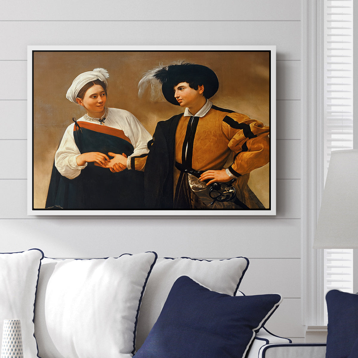The Fortune Teller (Capitoline Version), c. 1599 by Caravaggio displayed above a sofa in a living room in a white floater frame, featuring a fortune teller tricking young man during palm reading.