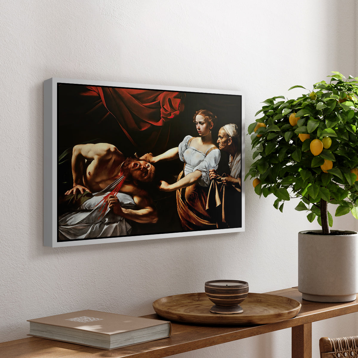 Judith Beheading Holofernes, c. 1599 by Caravaggio, presented in a white floater framed canvas featuring Judith cutting off Holofernes' head as maidservant assists beside her, displayed above a hallway console table.