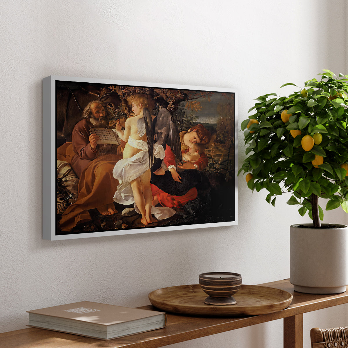 Rest on the Flight into Egypt, c. 1597 by Caravaggio, presented in a white floater framed canvas featuring the Holy Family resting in landscape with angel playing violin, displayed above a hallway console table.