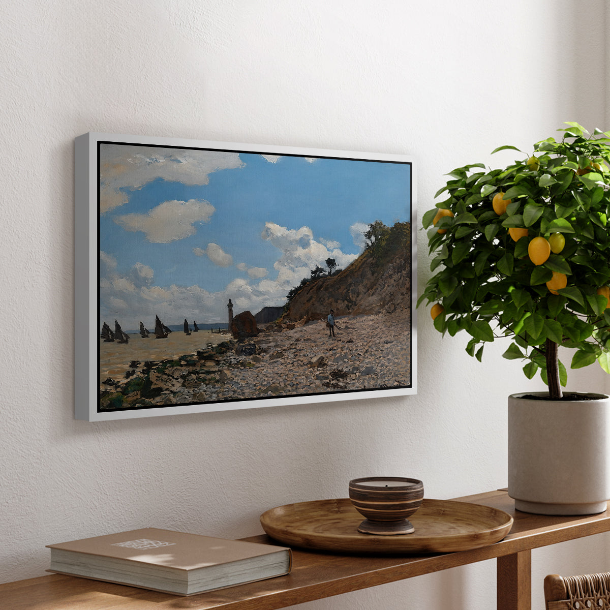 The Beach at Honfleur, 1864 by Claude Monet, presented in a white floater framed canvas featuring a coastal beach scene with figures gathered along shoreline and boats nearby, displayed above a hallway console table.