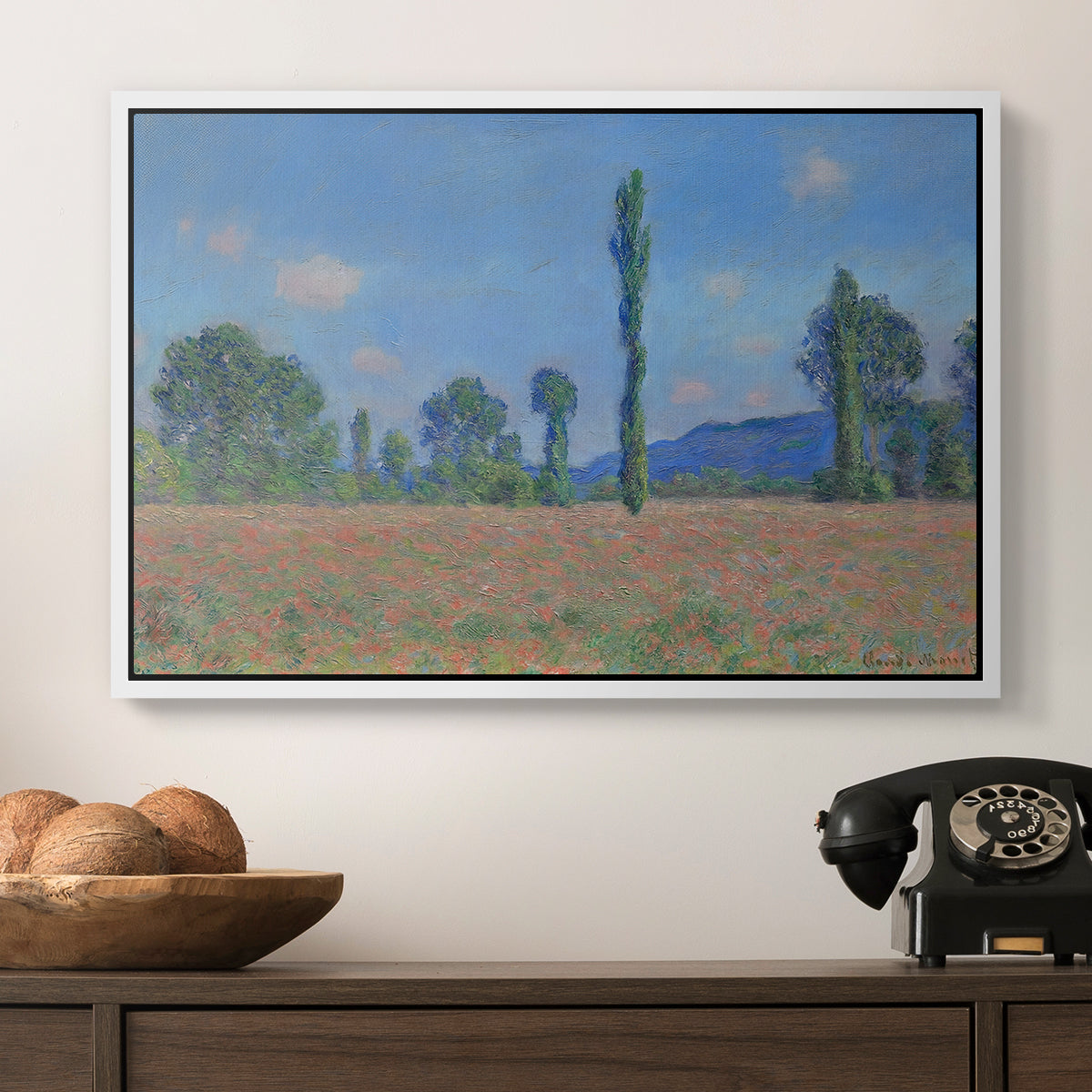 Poppy Field (Giverny), 1890-1891 by Claude Monet in a white floater framed canvas displayed above a console table in a hallway, featuring a rural field filled with red blossoms beneath open sky.