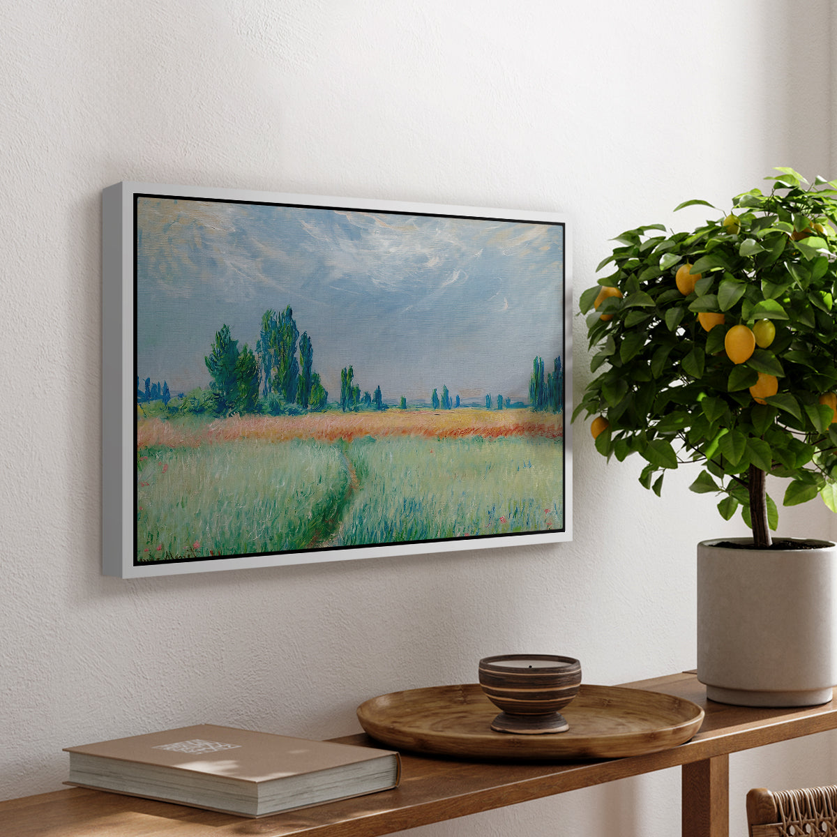 The Wheat Field (Champ de Blé), 1881 by Claude Monet, presented in a white floater framed canvas featuring a golden wheat field stretching across landscape under soft sky, displayed above a hallway console table.