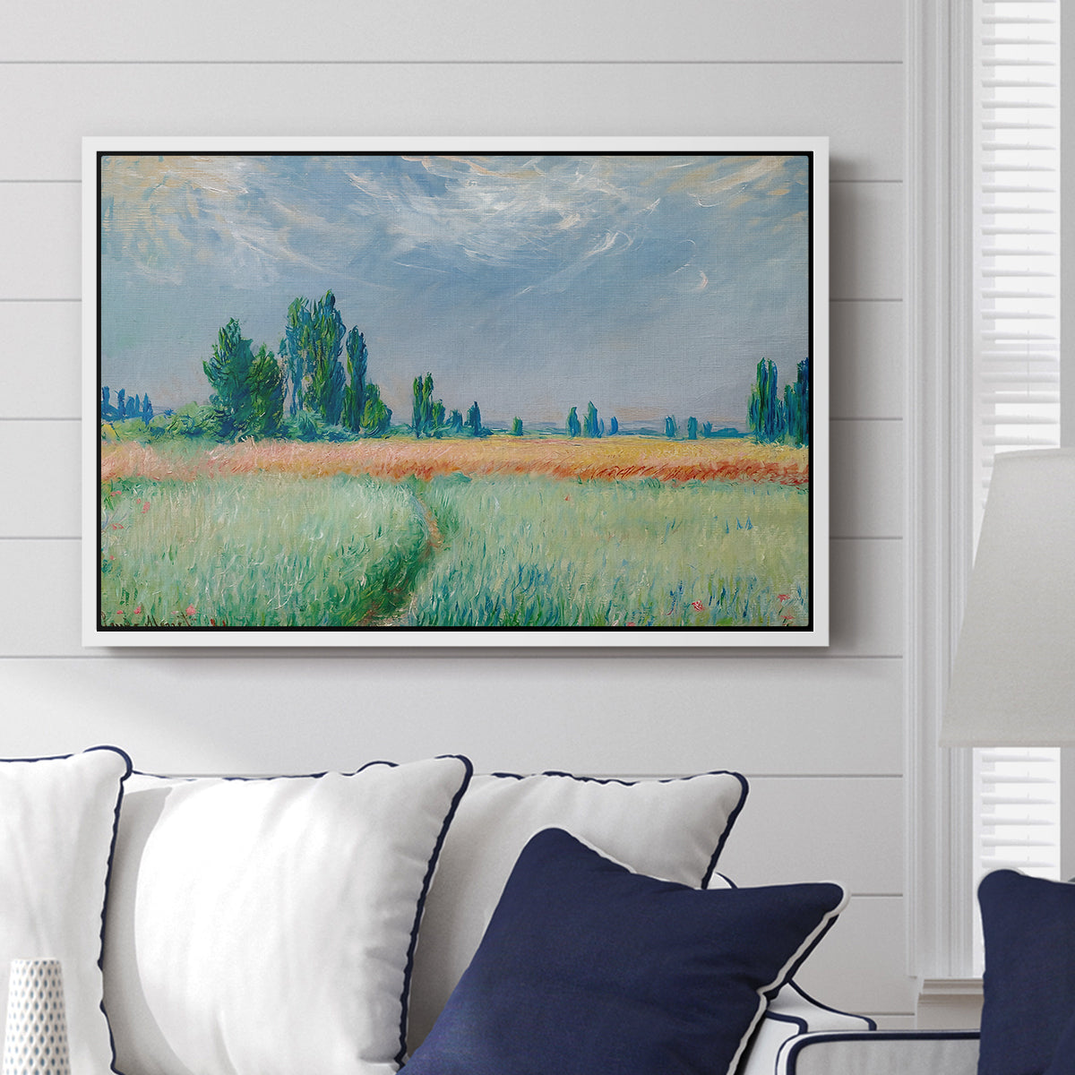 The Wheat Field (Champ de Blé), 1881 by Claude Monet displayed above a sofa in a living room in a white floater frame, featuring an impressionist depiction of ripened grain field in countryside.