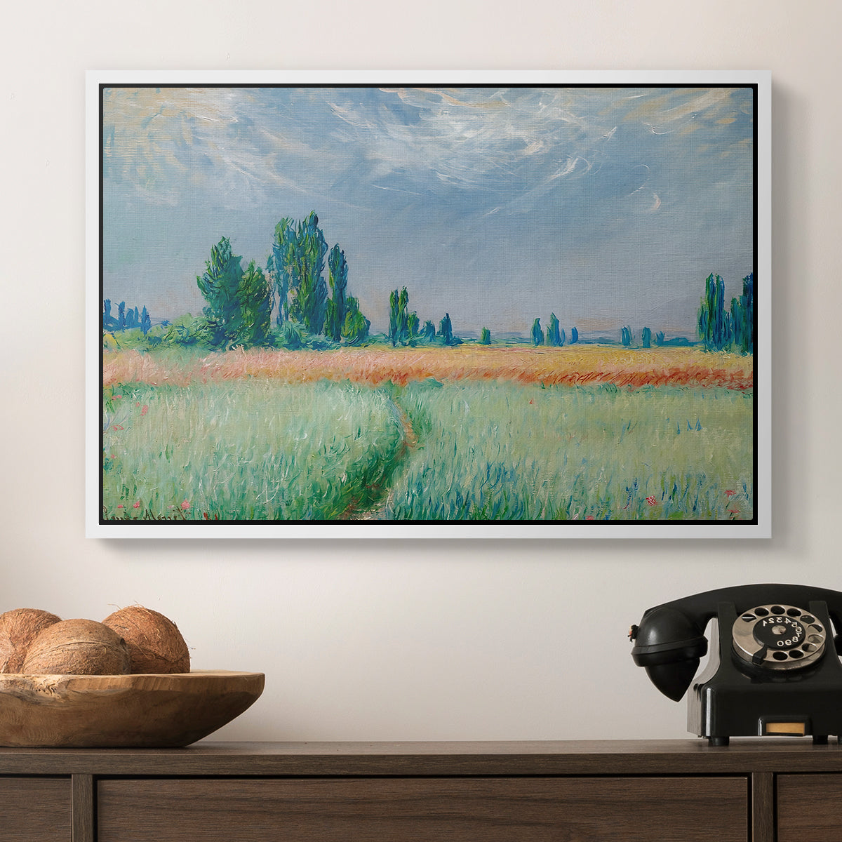 The Wheat Field (Champ de Blé), 1881 by Claude Monet in a white floater framed canvas displayed above a console table in a hallway, featuring a serene rural scene with textured wheat under natural light.