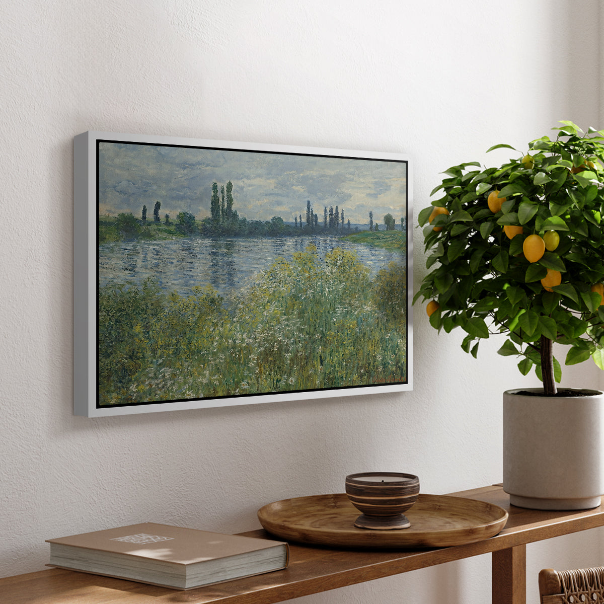 Banks of the Seine, Vétheuil, 1880 by Claude Monet, presented in a white floater framed canvas featuring a riverbank landscape with water, trees, and distant village buildings, displayed above a hallway console table.