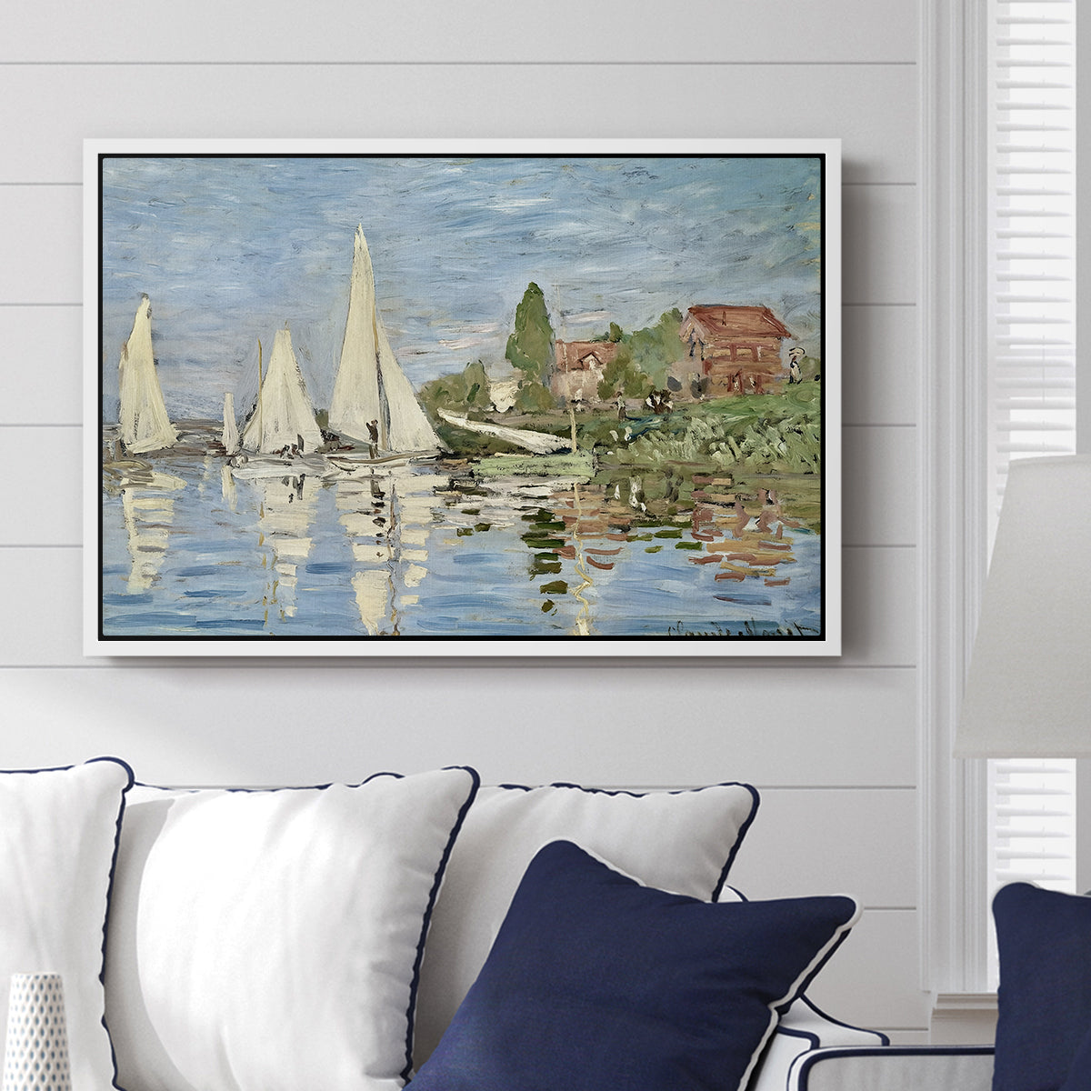 Regatta at Argenteuil, 1872 by Claude Monet displayed above a sofa in a living room in a white floater frame, featuring a lively regatta scene with multiple boats and fluttering sails.