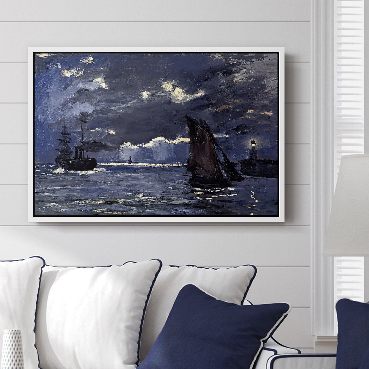 A Seascape, Shipping by Moonlight, 1864 by Claude Monet displayed above a sofa in a living room in a white floater frame, featuring a nocturnal seascape with boats silhouetted against glowing moon.