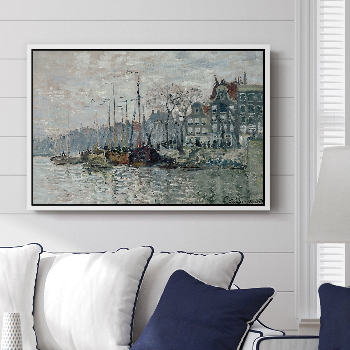 View of the Prins Hendrikkade and Kromme Waal in Amsterdam, 1874 by Claude Monet displayed above a sofa in a living room in a white floater frame, featuring an impressionist cityscape of canal with ships and architecture.