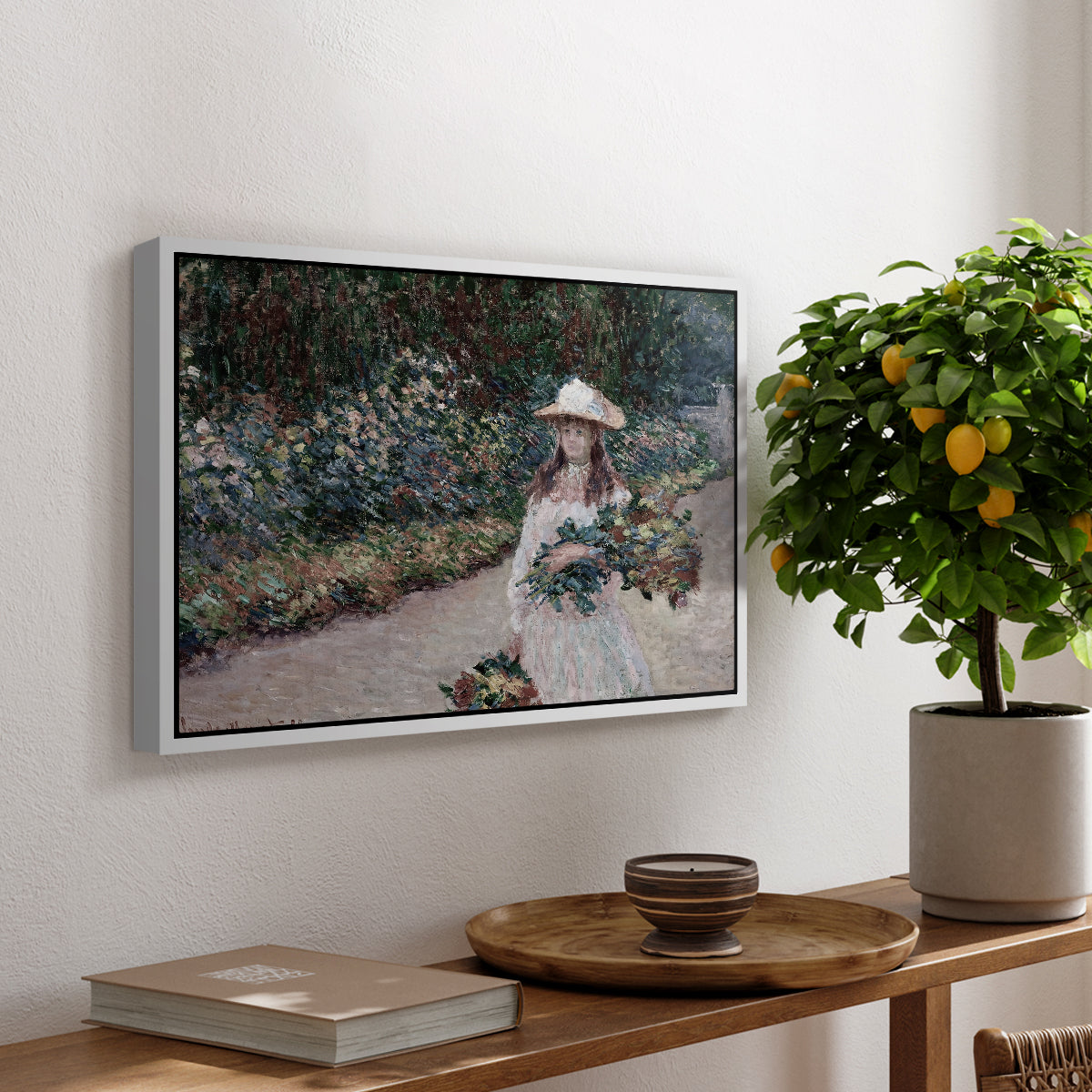 Young Girl in the Garden at Giverny, 1888 by Claude Monet, presented in a white floater framed canvas featuring a young girl seated in lush garden surrounded by blooming flowers, displayed above a hallway console table.