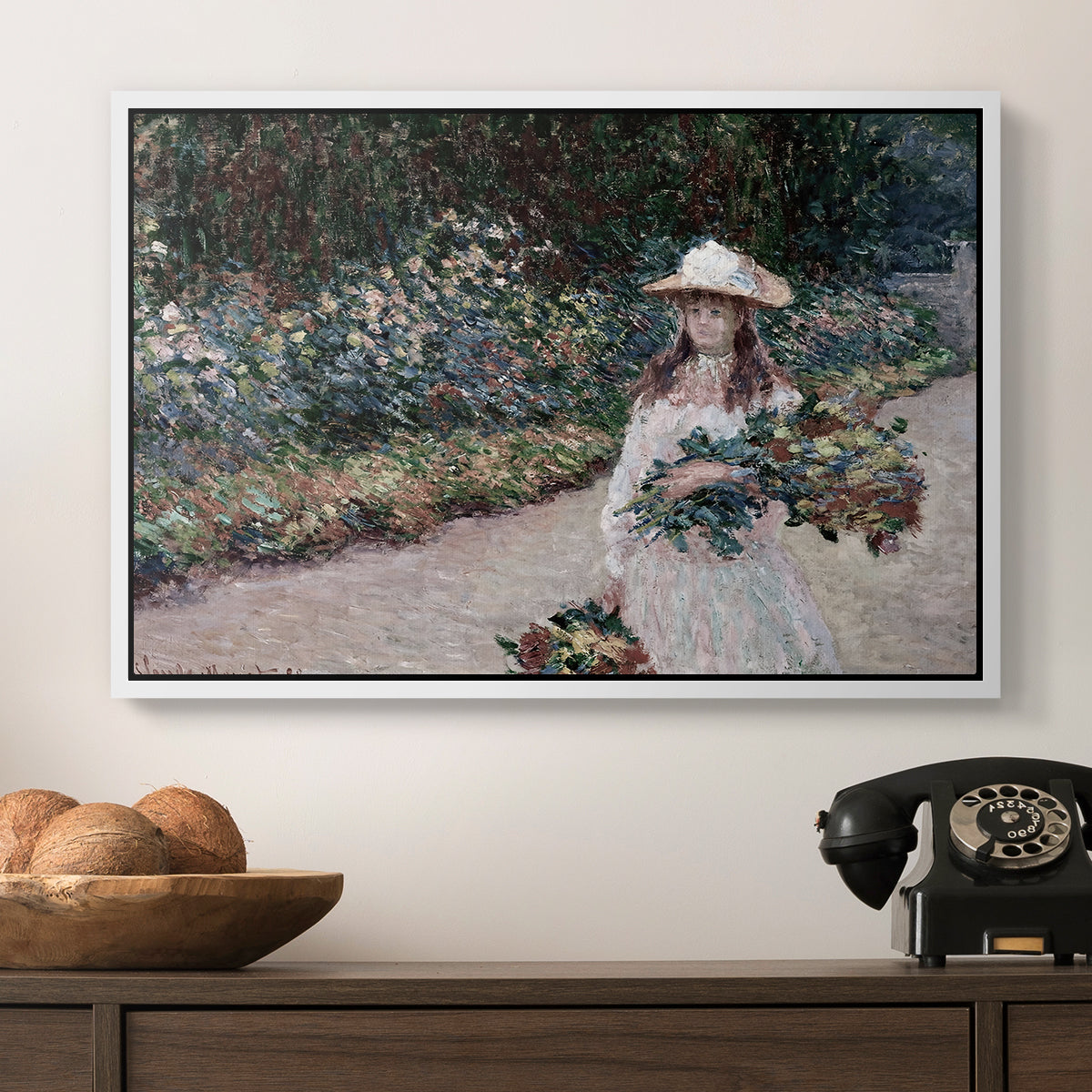 Young Girl in the Garden at Giverny, 1888 by Claude Monet in a white floater framed canvas displayed above a console table in a hallway, featuring a tranquil outdoor portrait of girl in floral setting.