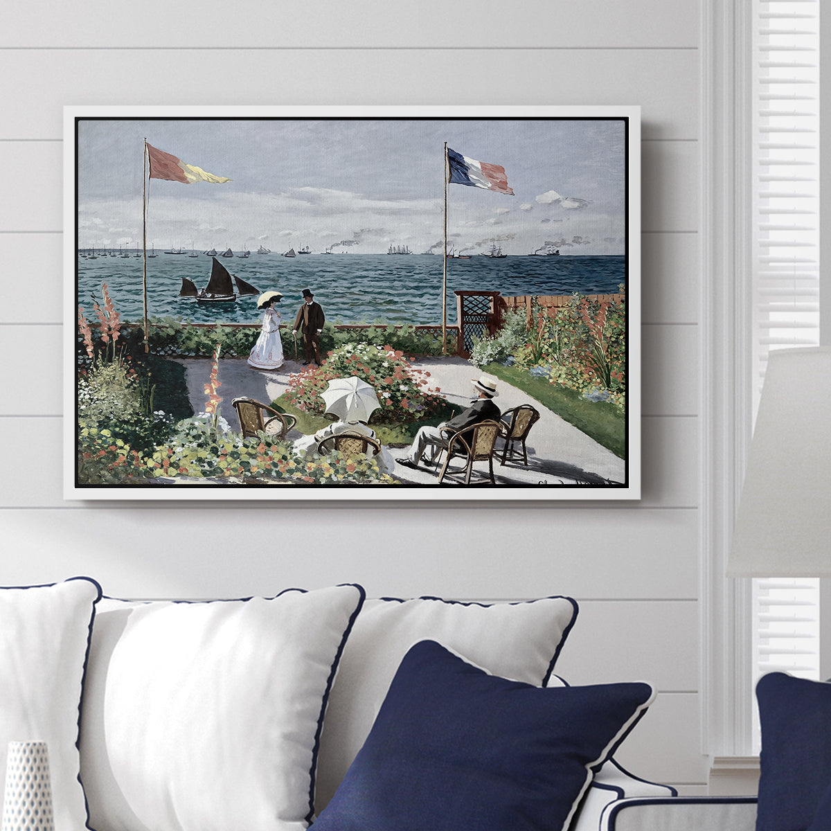 Garden at Sainte-Adresse, 1867 by Claude Monet displayed above a sofa in a living room in a white floater frame, featuring an impressionist coastal garden with people and ocean view.