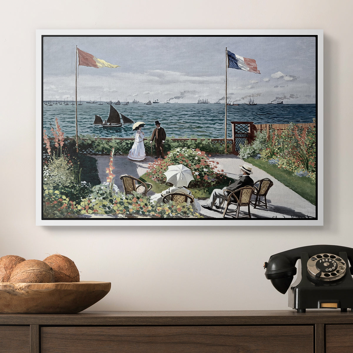 Garden at Sainte-Adresse, 1867 by Claude Monet in a white floater framed canvas displayed above a console table in a hallway, featuring a landscaped terrace with figures and flags near shoreline.
