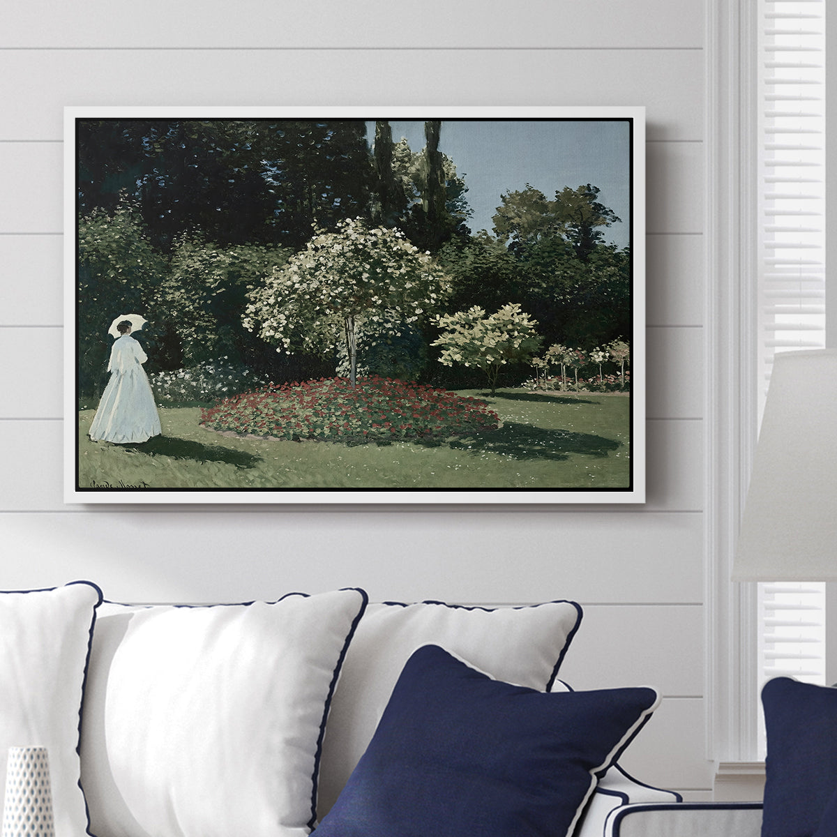 Woman in the Garden, Sainte-Adresse, 1867 by Claude Monet displayed above a sofa in a living room in a white floater frame, featuring an impressionist figure in sunlit garden with lush vegetation.