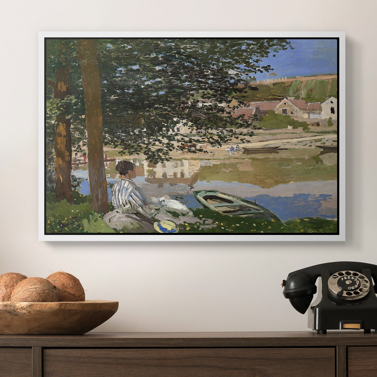 On the Bank of the Seine, Bennecourt, 1868 by Claude Monet in a white floater framed canvas displayed above a console table in a hallway, featuring a quiet outdoor setting with figures near river under foliage.