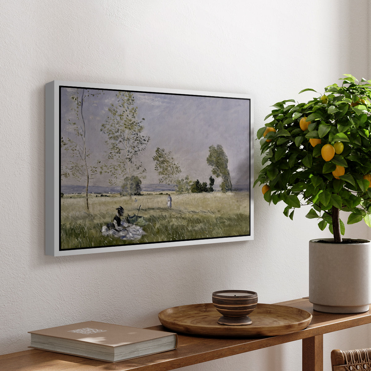 Summer (L'ete), 1874 by Claude Monet, presented in a white floater framed canvas featuring a woman seated in grassy field beneath tree in bright summer landscape, displayed above a hallway console table.