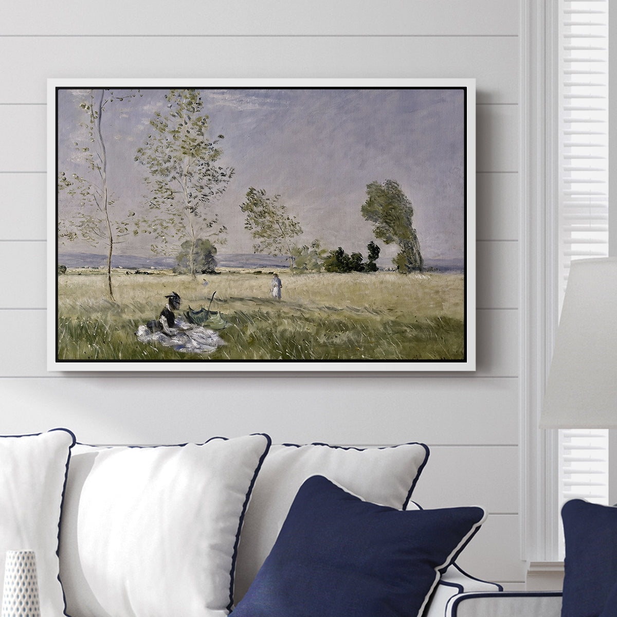Summer (L'ete), 1874 by Claude Monet displayed above a sofa in a living room in a white floater frame, featuring an impressionist countryside scene with figure resting in shade.