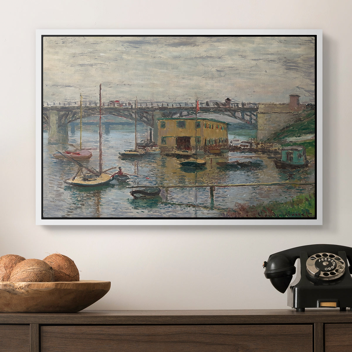 Bridge at Argenteuil on a Gray Day, c. 1876 by Claude Monet in a white floater framed canvas displayed above a console table in a hallway, featuring a subdued urban landscape with structure spanning river.