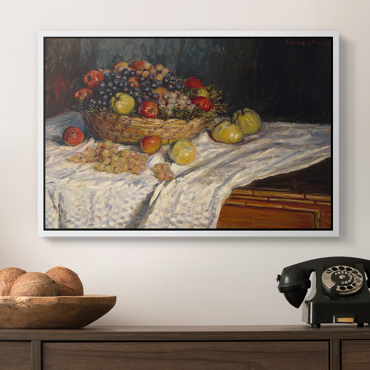 Still Life with Apples and Grapes, 1880 by Claude Monet in a white floater framed canvas displayed above a console table in a hallway, featuring a tabletop composition with fruit and subtle shadows.